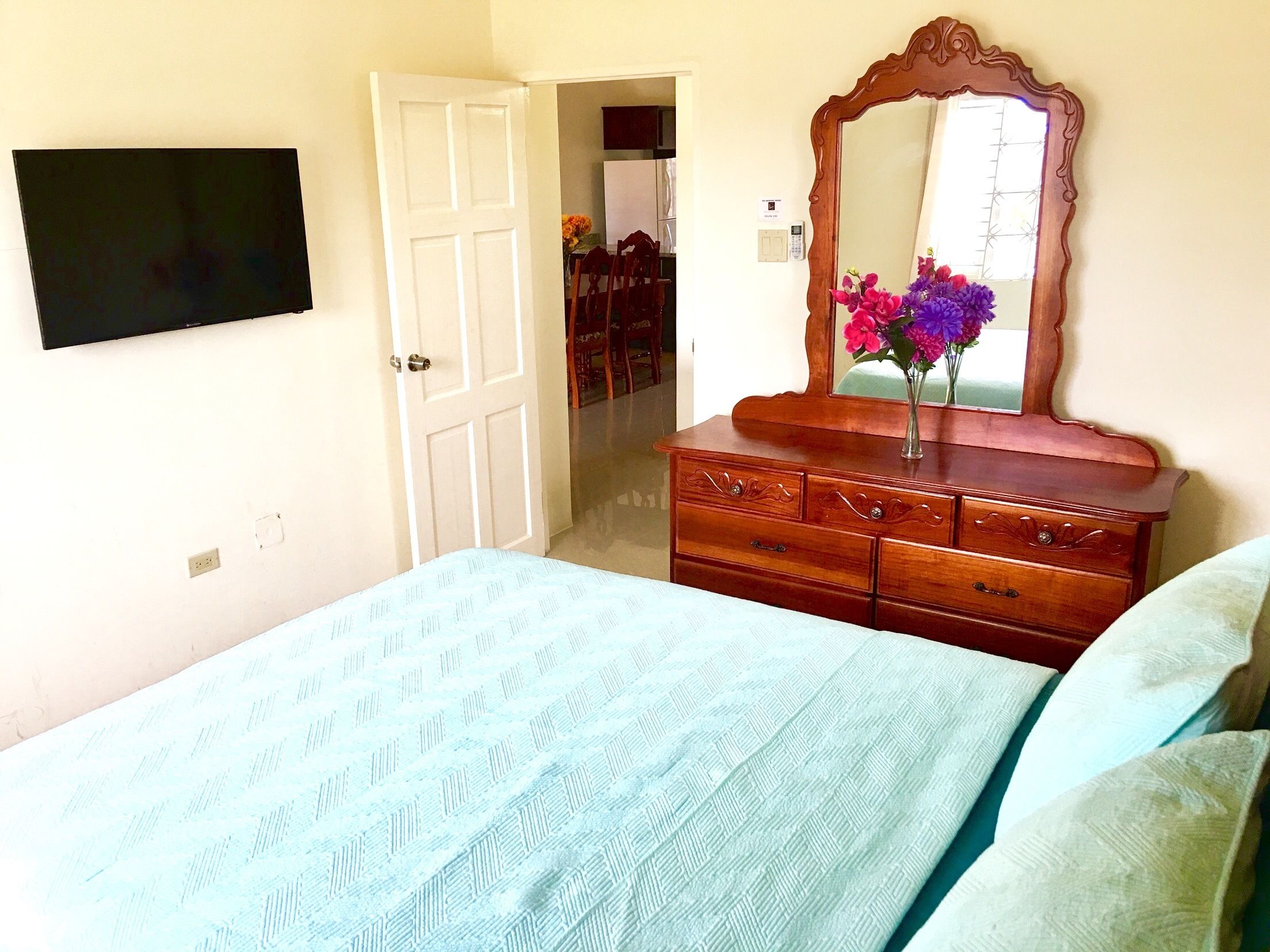 Ein Schlafzimmer mit Bett, Schminktisch, Spiegel und Fernseher an der Wand.