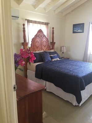 Un dormitorio con cabecera de madera, cama con colcha azul oscuro, mesita de noche con lámpara y un jarrón con flores.