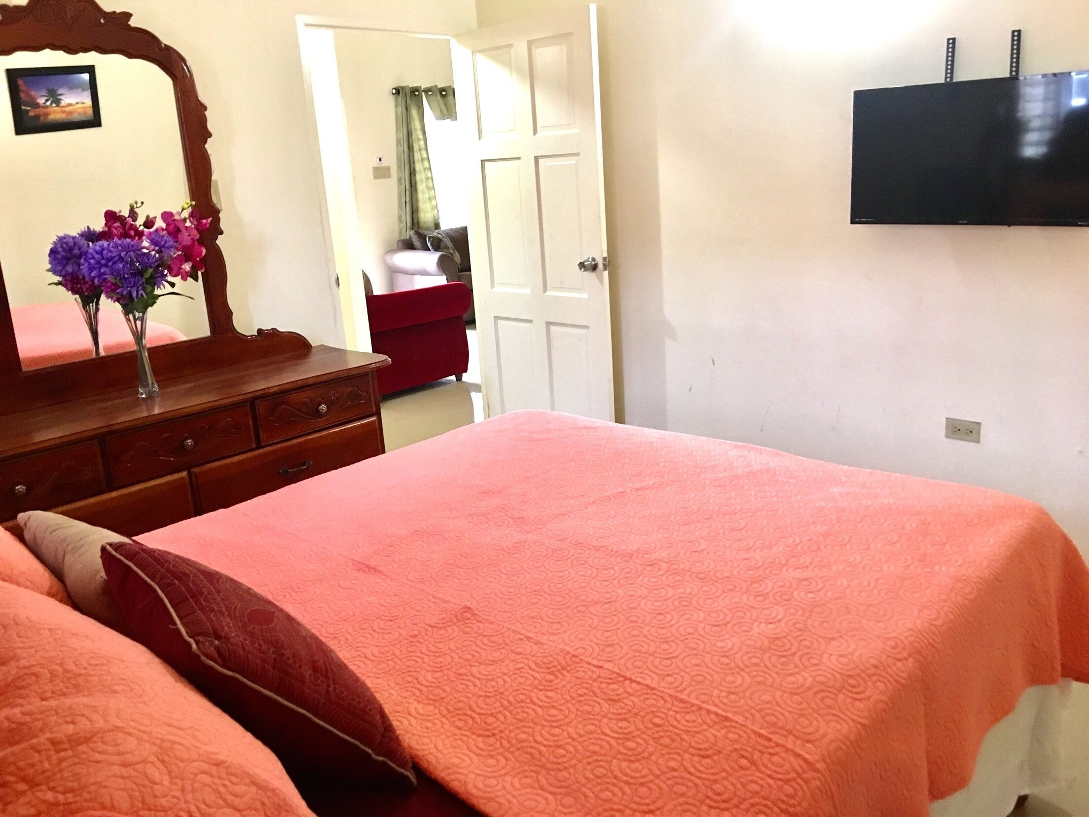 Une chambre à coucher avec un lit, une commode, un miroir et un téléviseur fixé au mur.