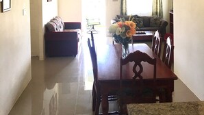 A spacious living area with a high ceiling, a dining table with chairs, a sofa, and a window with curtains. - Drax Hall Country Club's Sweet Escape (Ocho Rios)