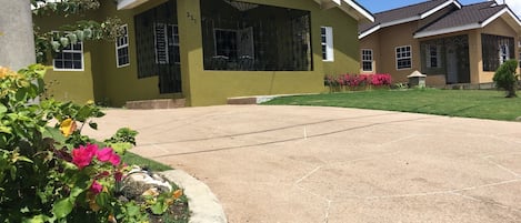 A residential house with a green exterior, large windows, and a paved driveway.