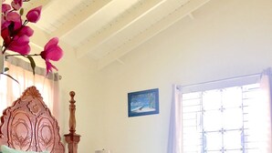 A bedroom with a bed, a wooden headboard, a nightstand, a lamp, a window with curtains, and a painting on the wall. - Drax Hall Country Club's Sweet Escape (Ocho Rios)