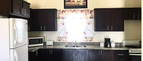 A kitchen with dark wooden cabinets, a white refrigerator, a microwave, a sink, and a stove.