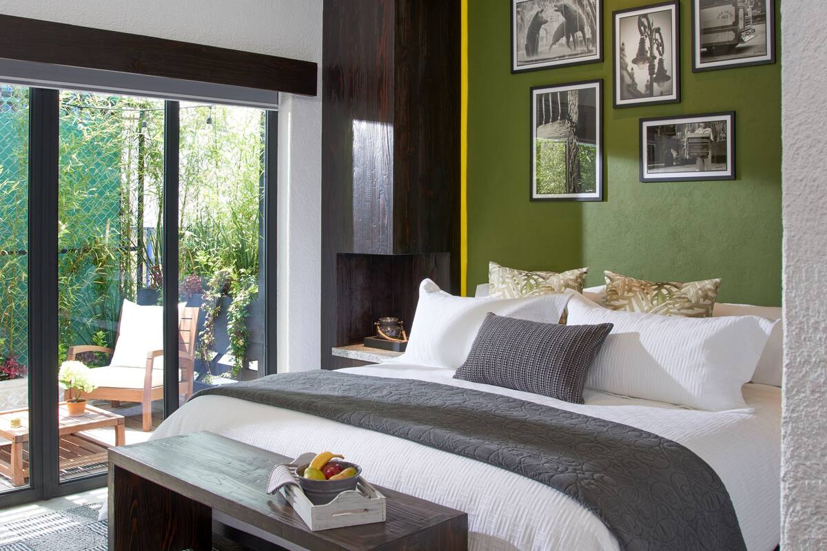A modern bedroom with a large bed, a wooden bench, and a view of greenery through a sliding door.