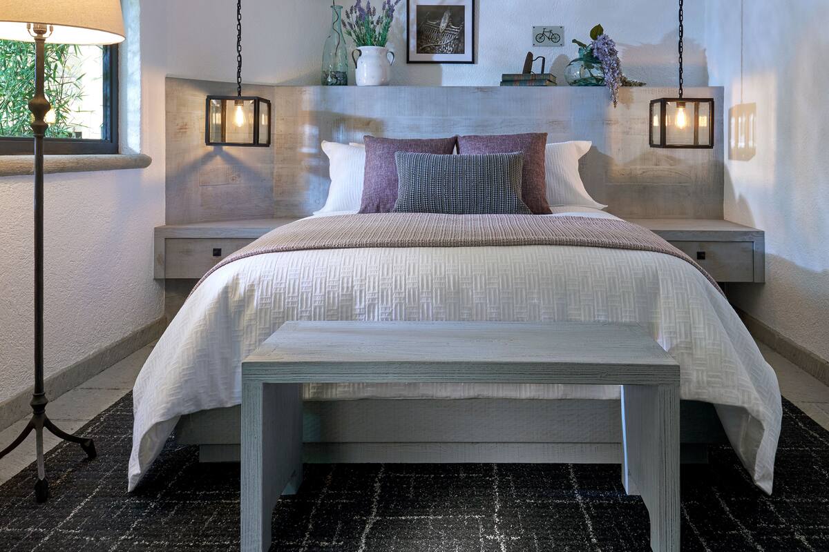 A bedroom with a bed, bedside tables, a bench, a lamp, and wall decorations.