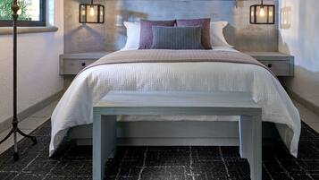 Un dormitorio con cama, mesitas de noche, un banco, una lámpara y adornos en la pared.