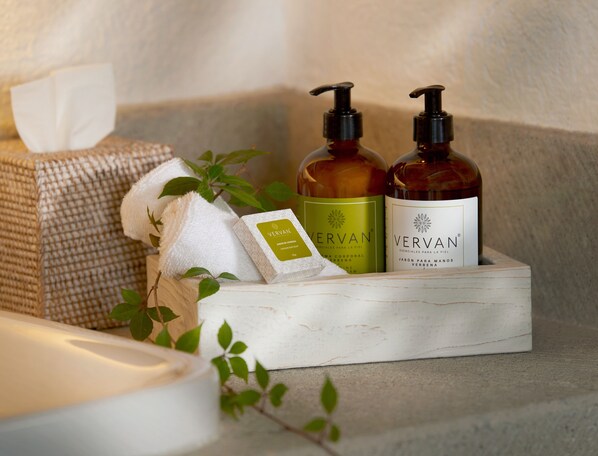 A wooden box containing two bottles of Vervan soap, a white towel, and a tissue box.