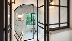 An open doorway leading to a bathroom with a marble floor, a wooden bench, and a view of greenery outside. - H21 Hospedaje Boutique (Mexico City)