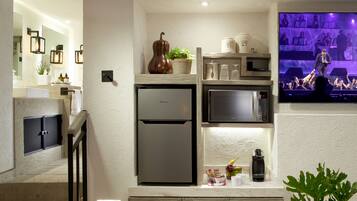 A modern kitchen with a Hisense refrigerator, a microwave, and a coffee maker. There is a small plant on the counter and a TV mounted on the wall displaying a concert.