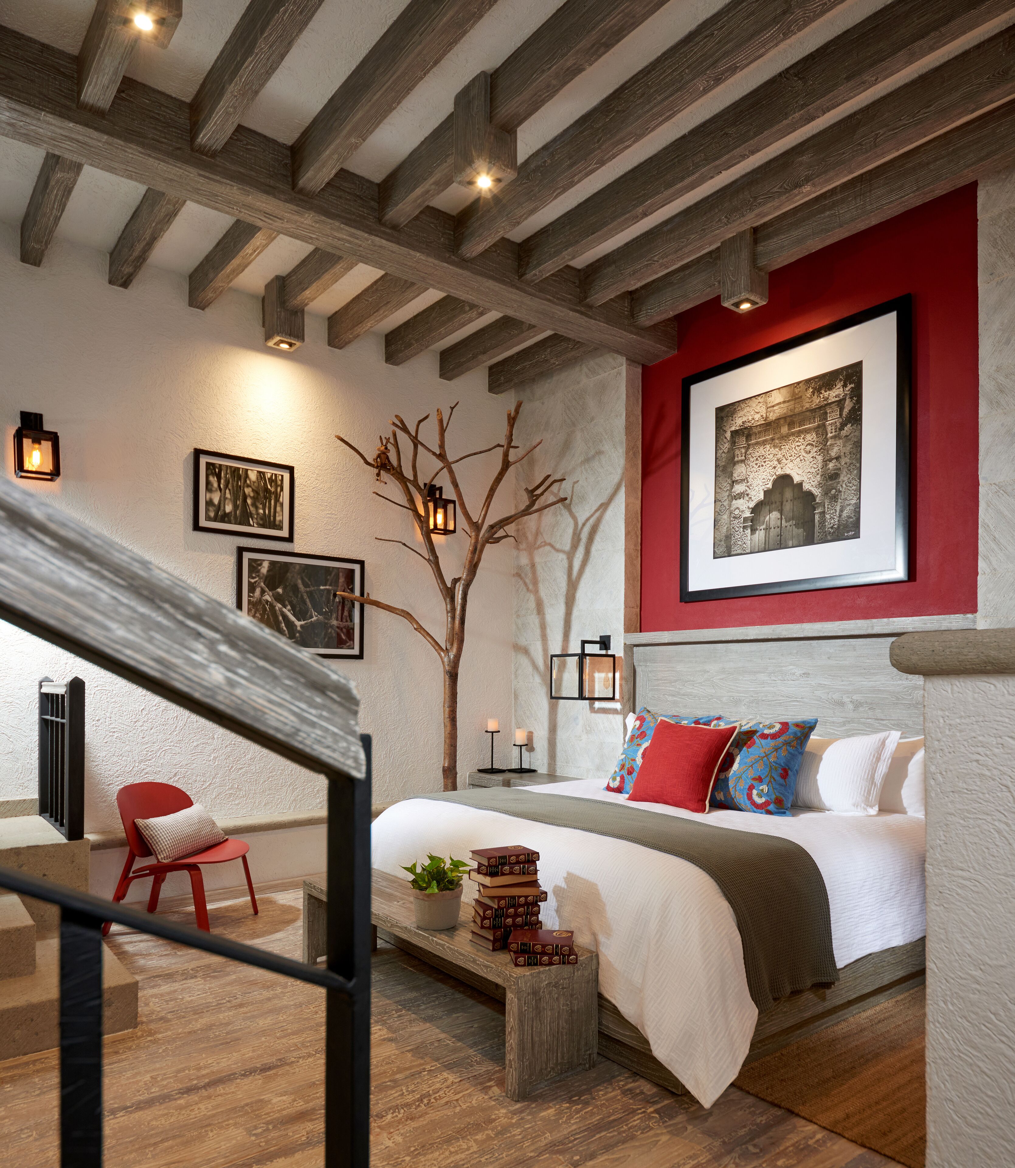 A bedroom with a bed, a red chair, a wooden bench, a potted plant, and a wall-mounted picture.