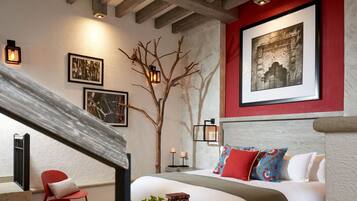 A bedroom with a bed, a red chair, a wooden bench, a potted plant, and a wall-mounted picture.