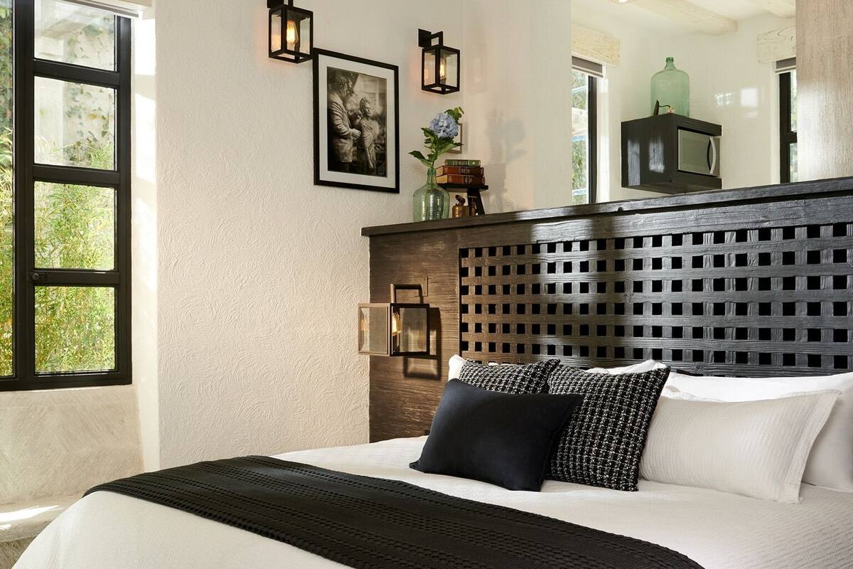 A bedroom with a large bed, a wooden headboard, a window, and wall-mounted lights.