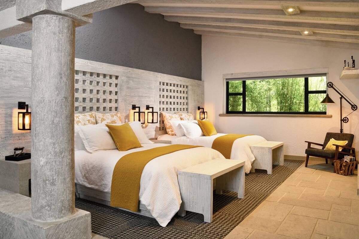 A modern bedroom with two beds, a large window, and a stone pillar.