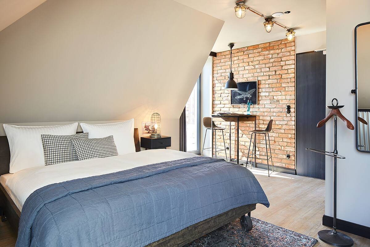A modern bedroom with a large bed, a brick accent wall, and a hanging light fixture.
