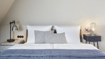 A neatly made bed with white and black checkered pillows, a blue blanket, and a nightstand with a lamp and a vintage light fixture.