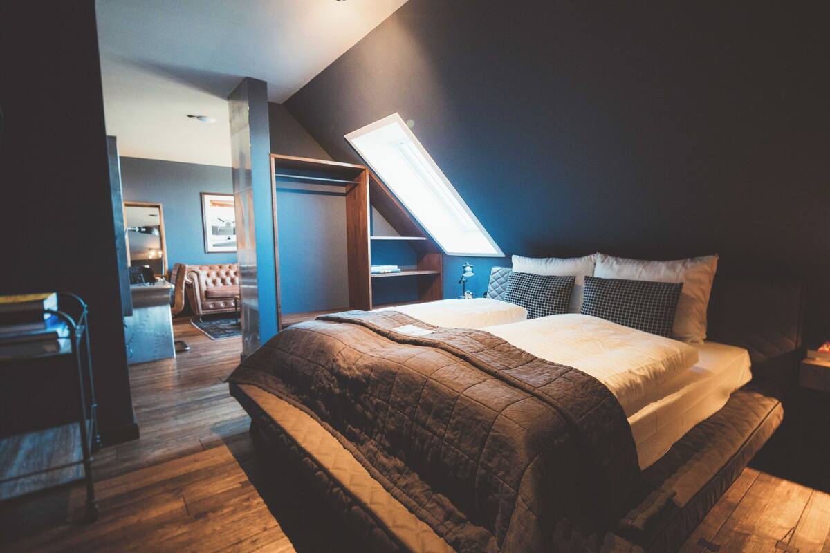 A bedroom with a large bed, a skylight, a wardrobe, and a desk.