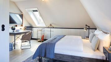 A modern bedroom with a large bed, a desk, and a computer. There is a skylight above the bed, and a lamp on the desk.