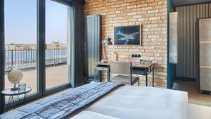 A hotel room with a large bed, a desk with a chair, a globe, and a view of the city through large windows. - Hotel Fliegerdeich (Wilhelmshaven)
