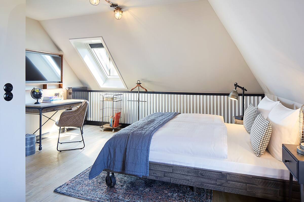 A bedroom with a bed, desk, chair, and a skylight.