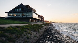 A modern house with a glass facade, located near a rocky shoreline. - Hotel Fliegerdeich (Wilhelmshaven)