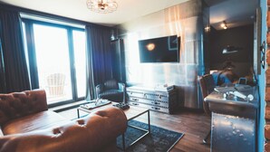 A modern living room with a leather sofa, a wooden coffee table, a television, and a vintage suitcase. - Hotel Fliegerdeich (Wilhelmshaven)