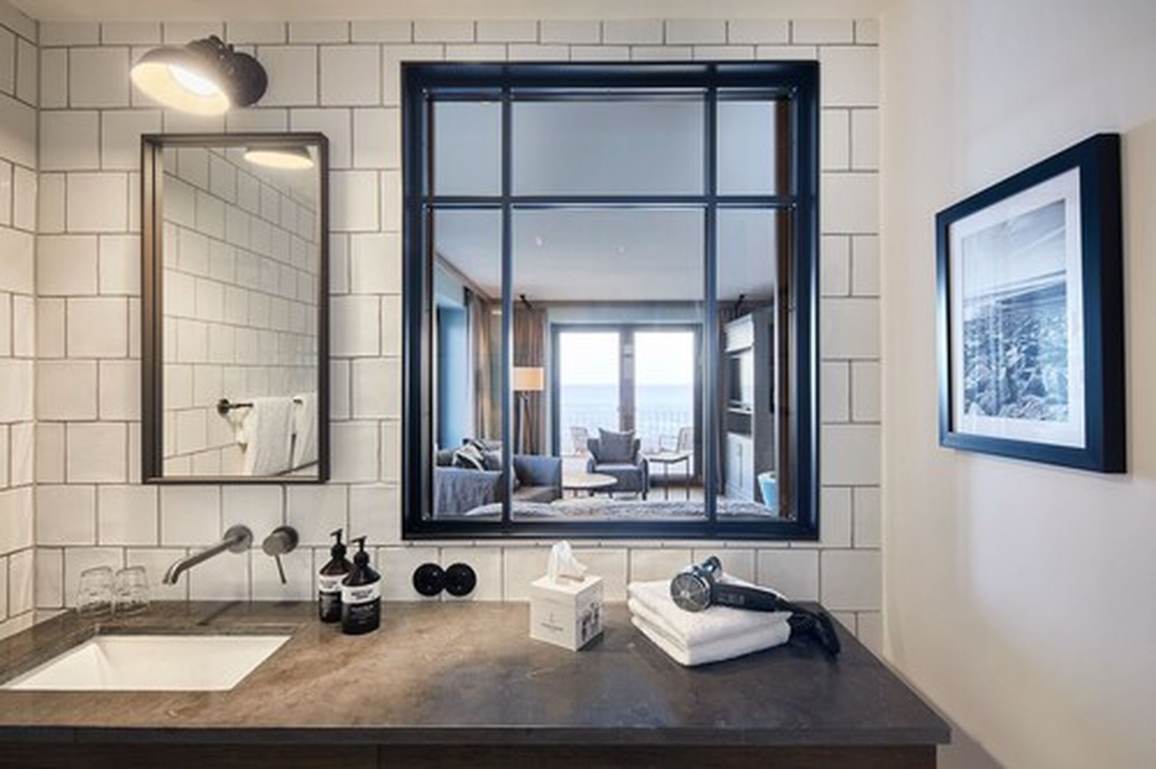 A modern bathroom with a large window, a mirror, a sink, and toiletries.