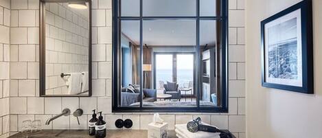 A modern bathroom with a large window, a mirror, a sink, and toiletries.