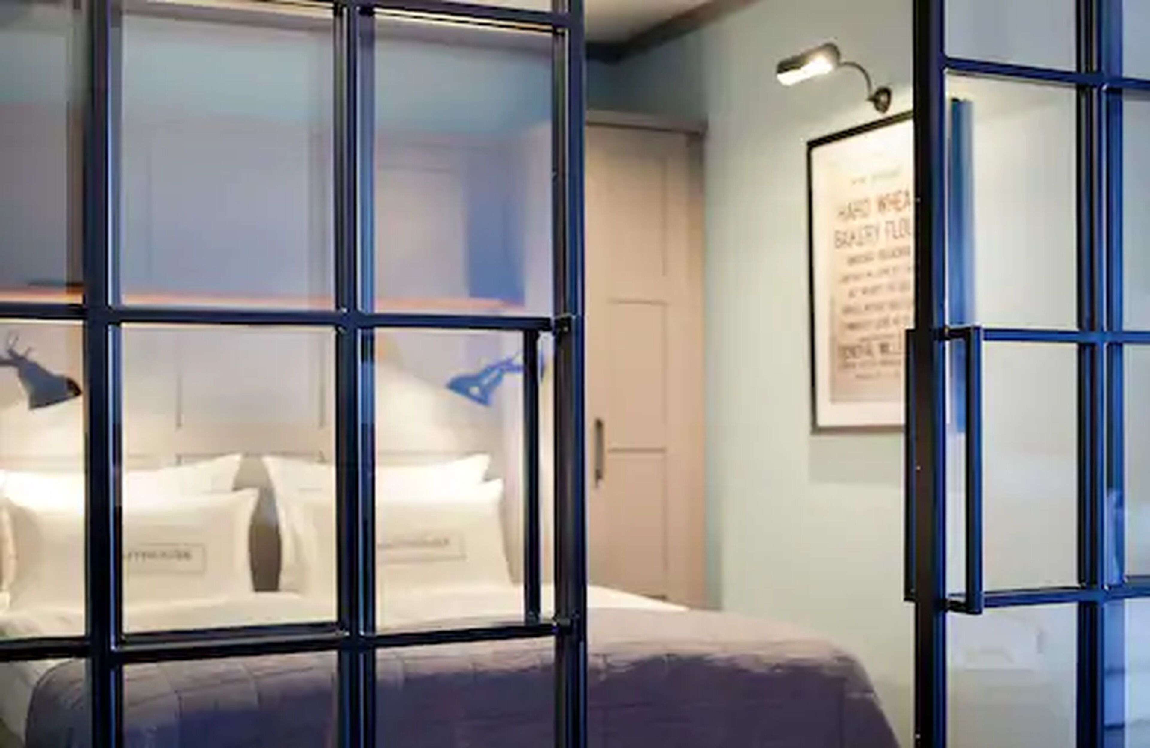 A hotel room with a large window, a bed with white linens, and a framed picture on the wall.