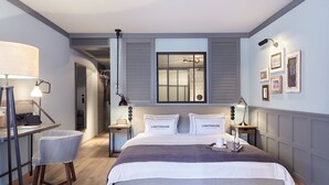 A modern bedroom with a large bed, two bedside tables, a desk with a chair, and a window with a view of the bathroom. - Lighthouse Hotel & SPA (Büsum)