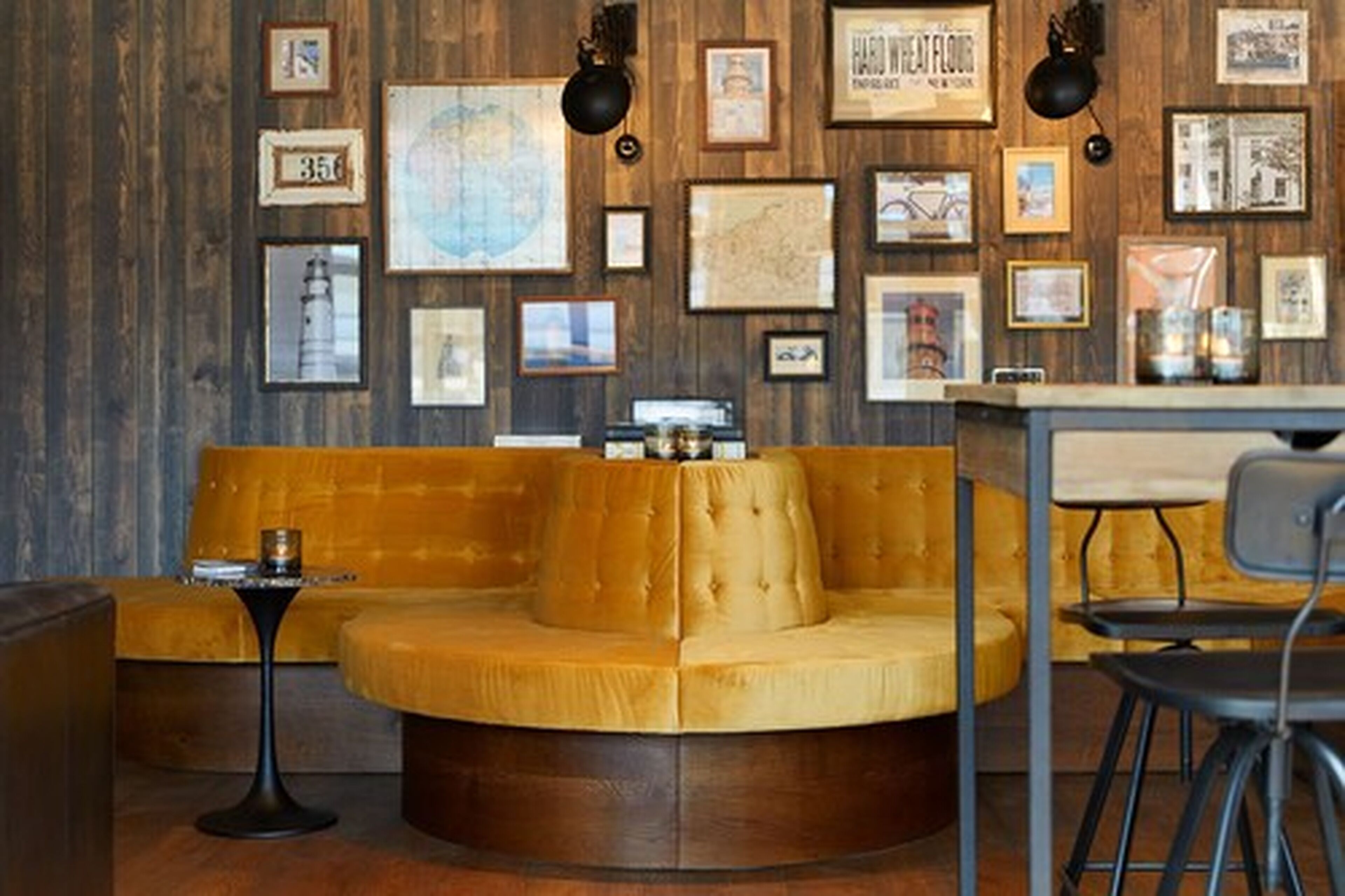 A cozy seating area with a round, tufted sofa and a small table, surrounded by framed pictures and maps on the wall.