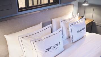 Una cama impecablemente arreglada con sábanas y almohadas blancas, cada una con la etiqueta 'Lighthouse Hotel & Spa'.