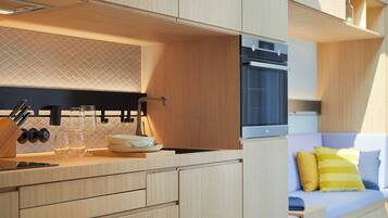 A modern kitchen with wooden cabinetry, a built-in oven, and a dining area with a sofa and cushions.