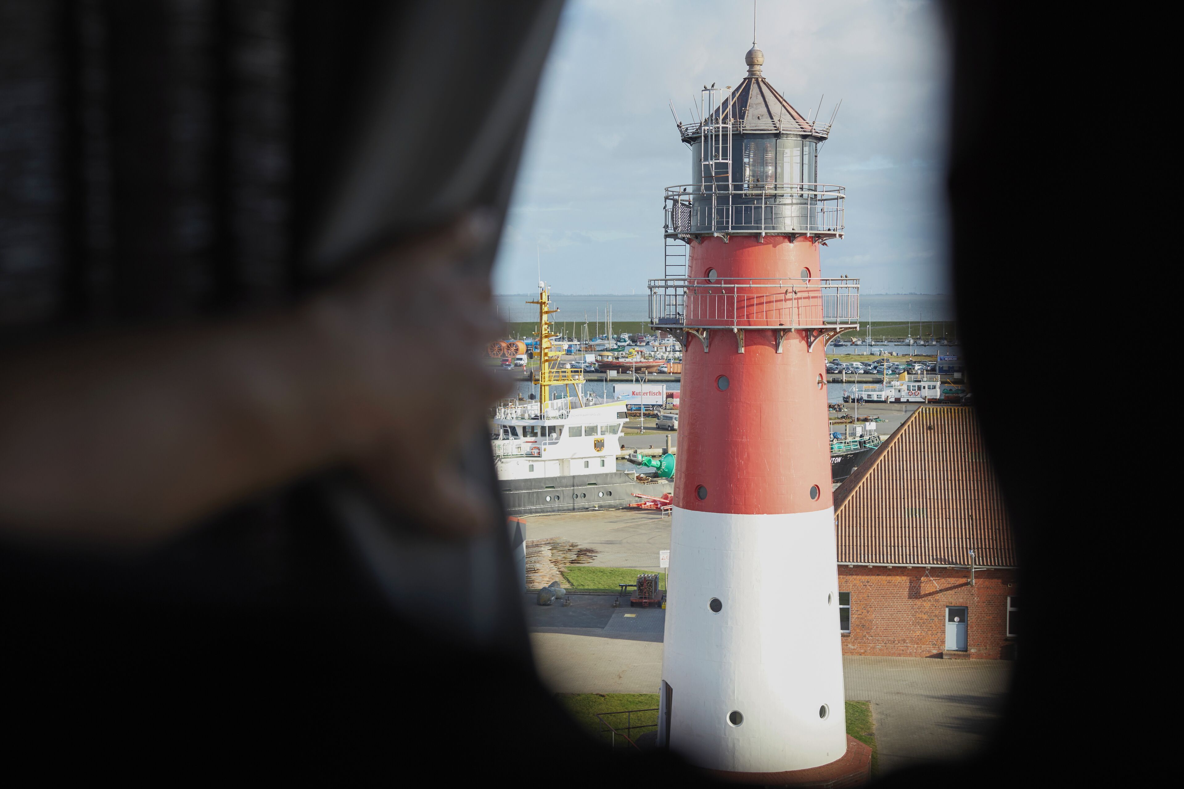 A lighthouse with a red and white structure, a brick building, and a marina with boats.