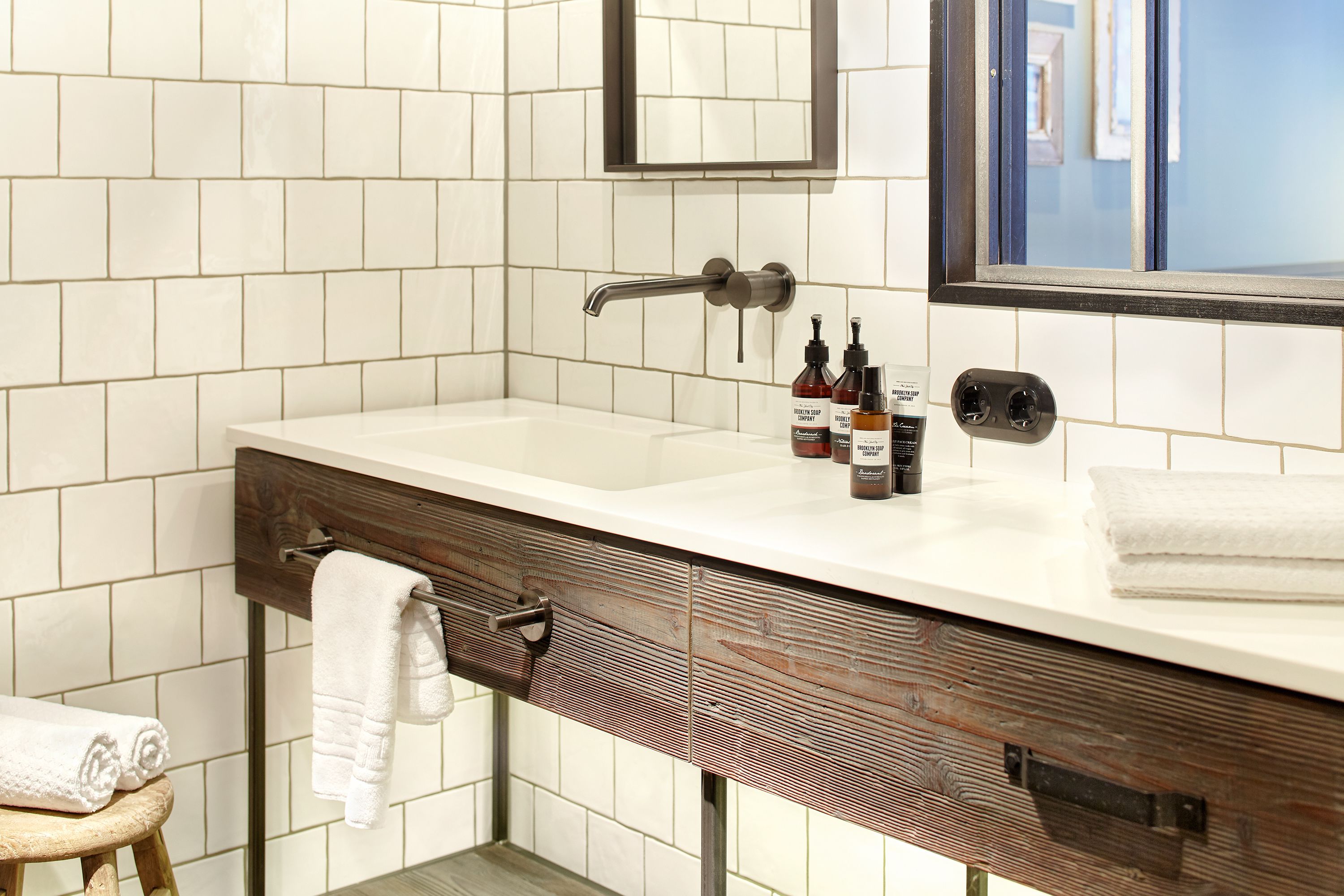 A bathroom with a white tiled wall, a wooden vanity with a towel rack, and a mirror above the sink.