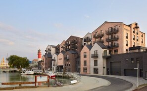 A waterfront residential building with multiple balconies, a marina with boats, and a lighthouse in the background.