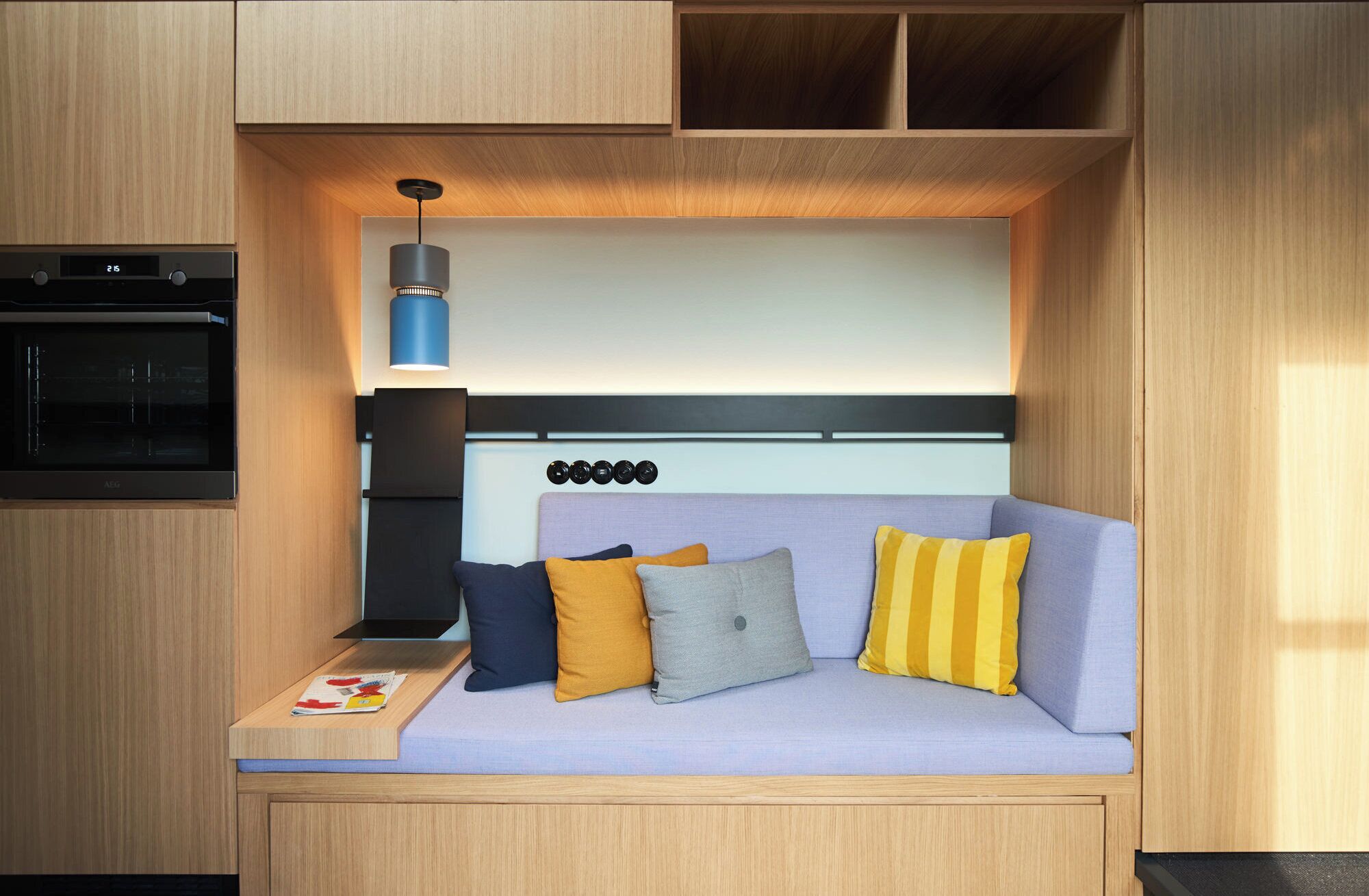 A compact kitchenette with a built-in oven and a small table with a magazine.