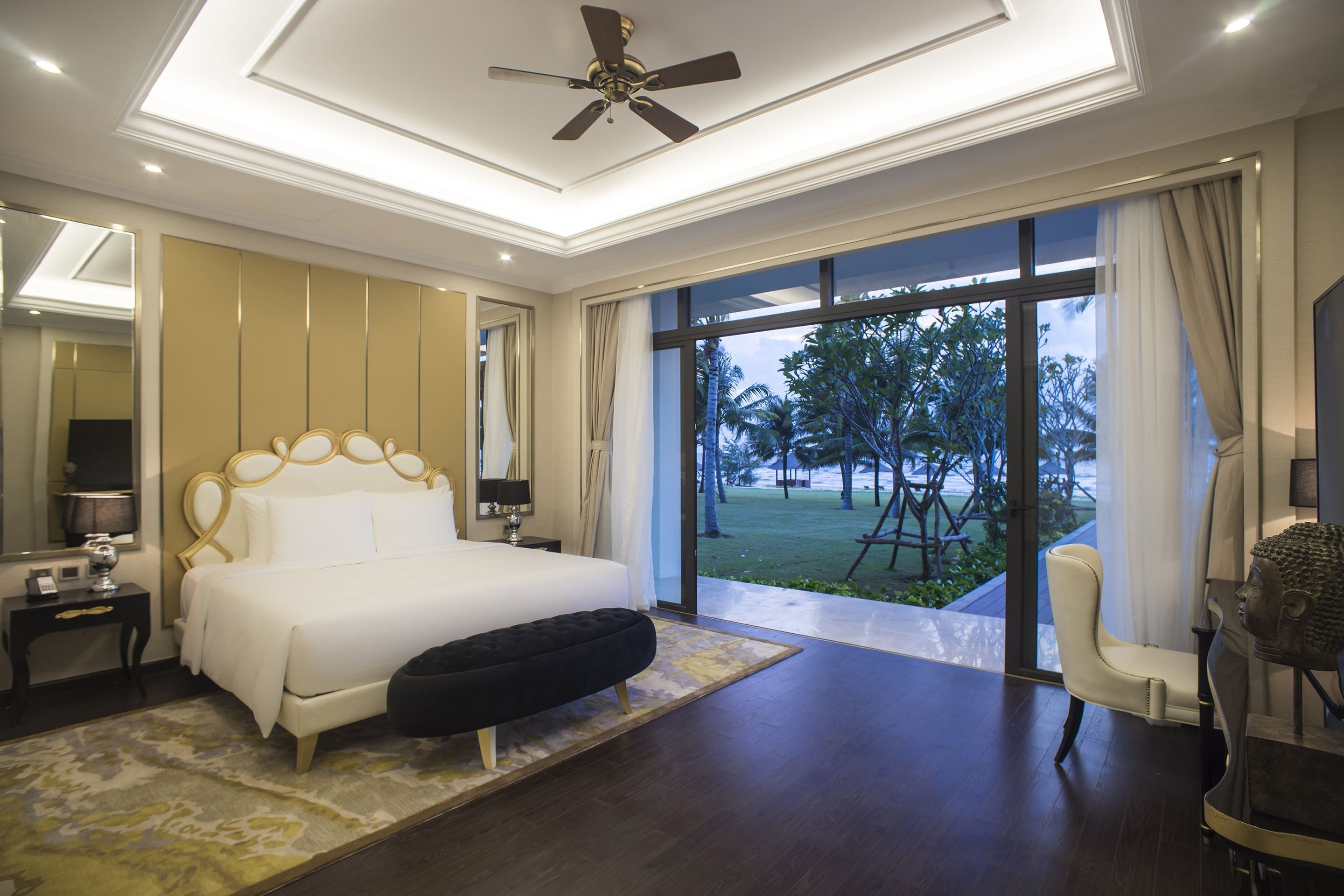 A modern bedroom with a large bed, a ceiling fan, and a view of the outdoors.