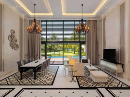 Amplia sala de estar con comedor, televisor y vistas a una piscina y vegetación.