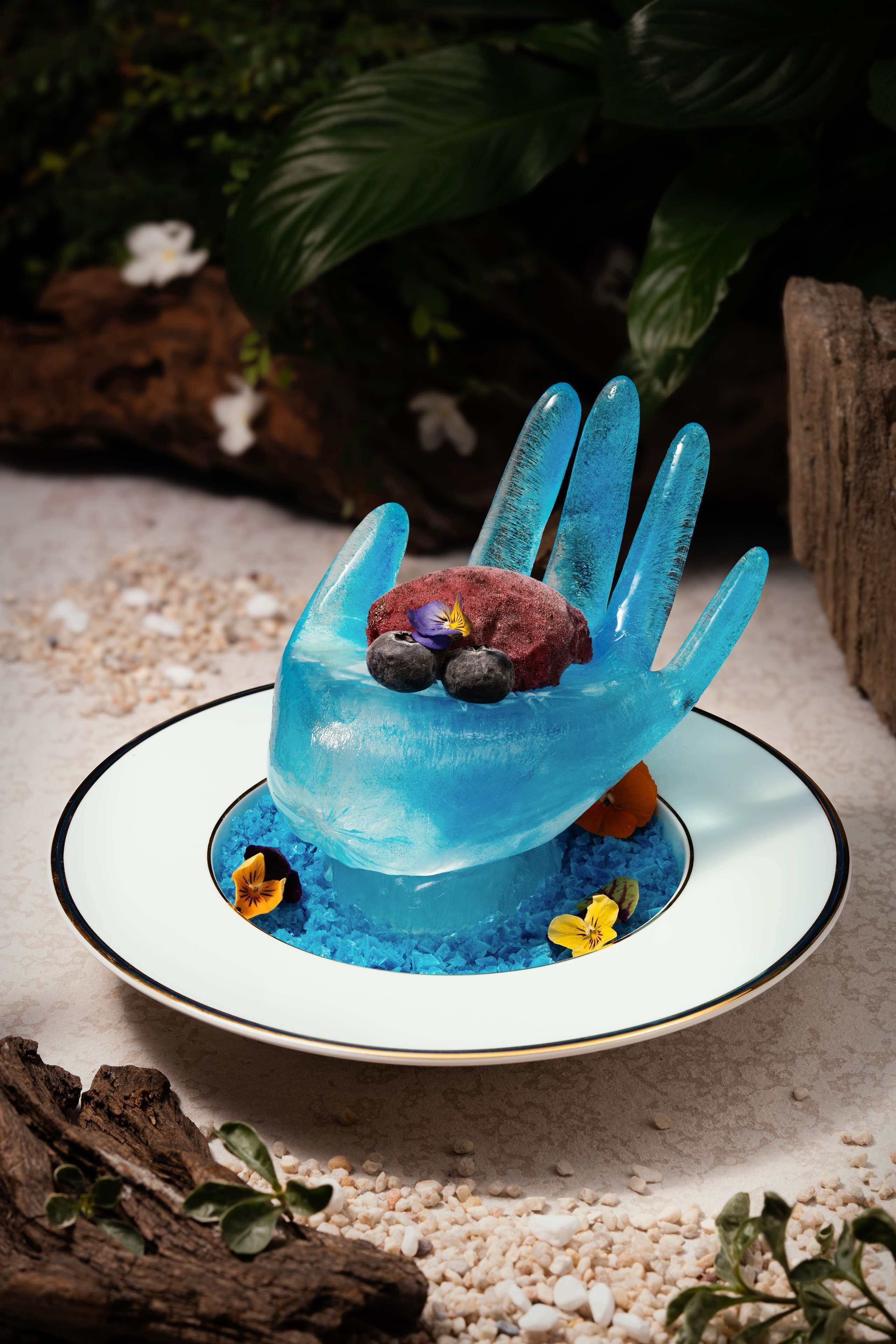 Ein Dessert auf einem Teller mit blauer Handabdruck-Dekoration, umgeben von kleinen Blumen und Beeren.