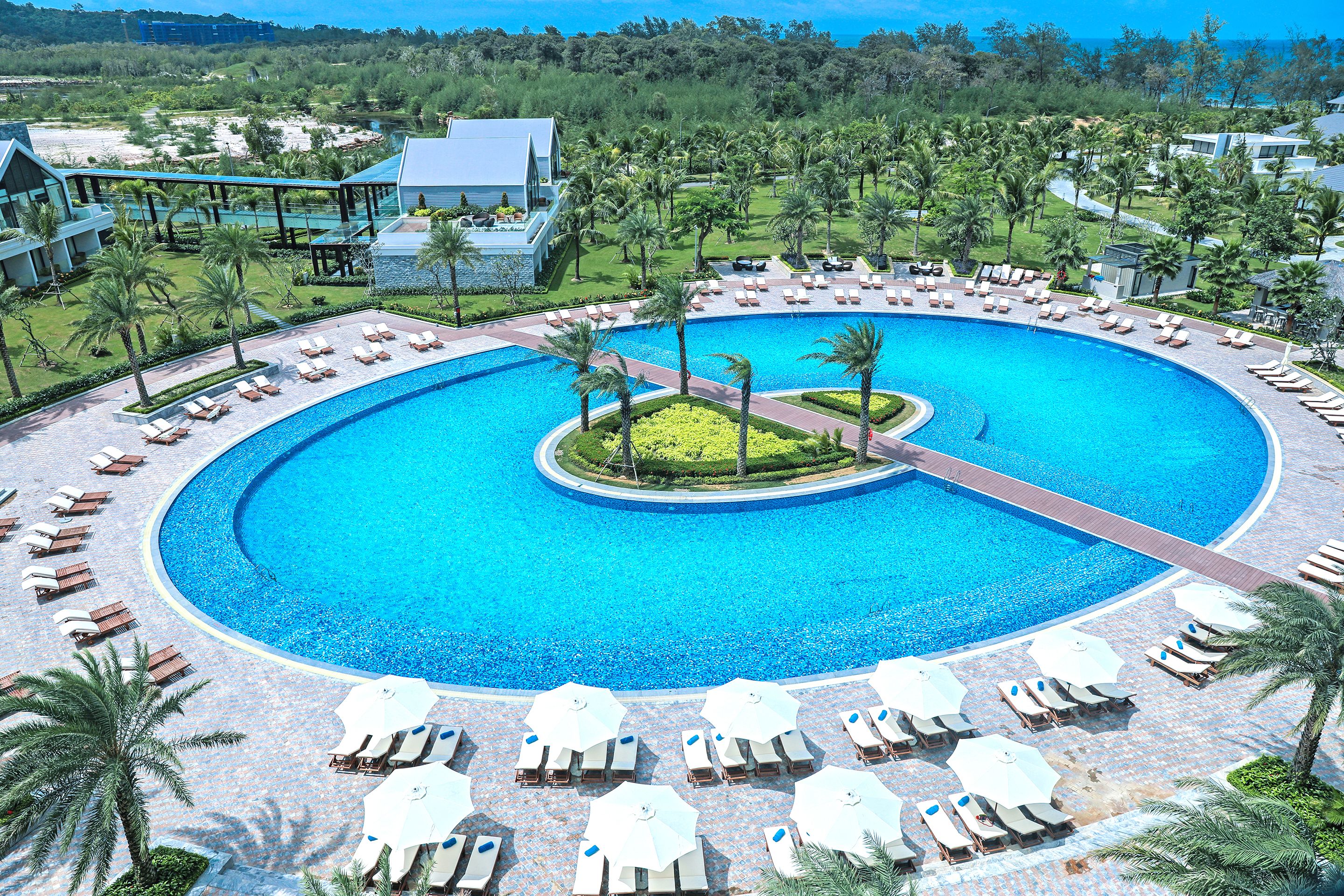 A resort with a large circular pool, sun loungers, and palm trees.