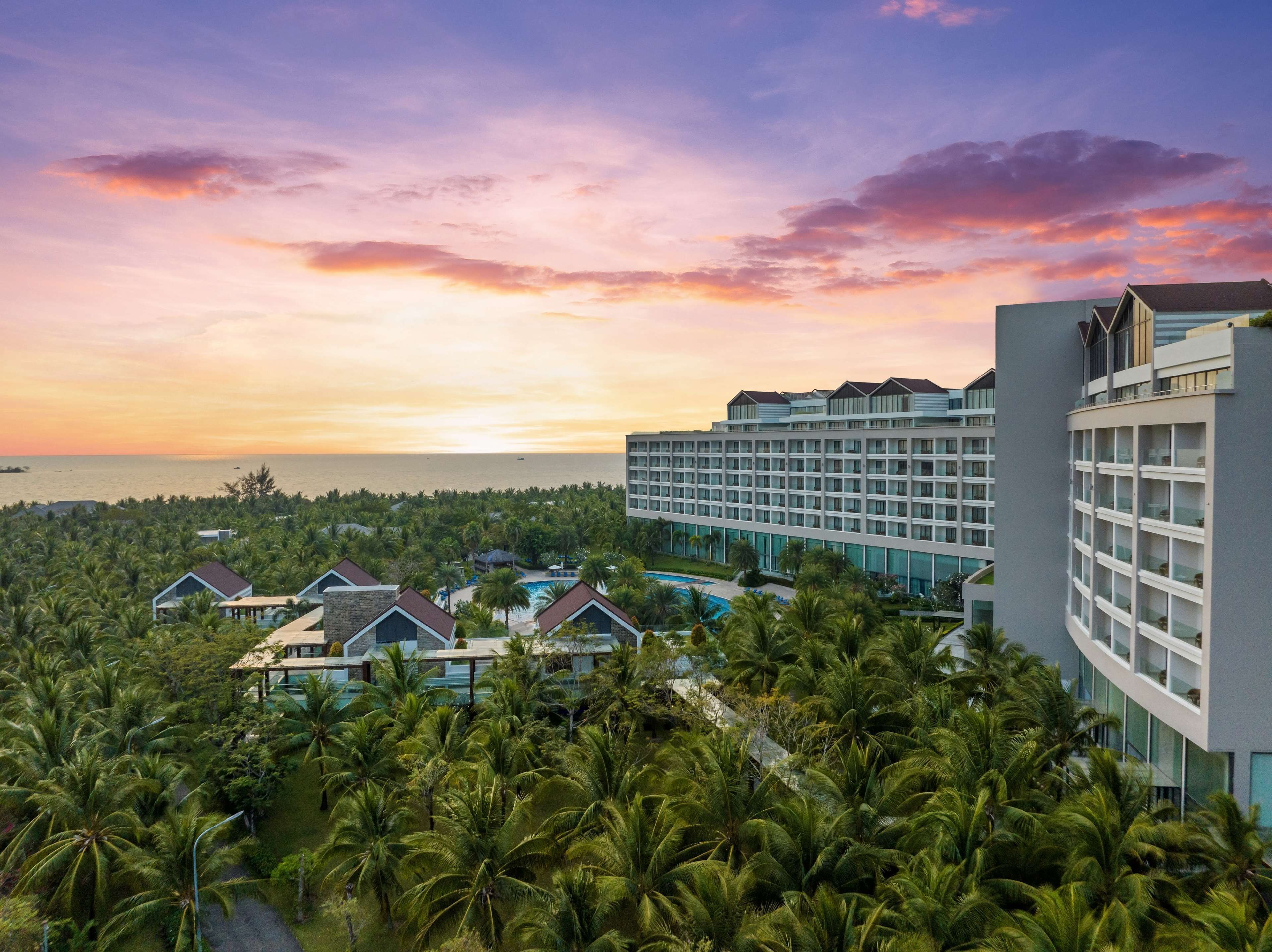 Un resort con un edificio grande, una piscina y palmeras frondosas.
