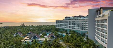 Un resort con un edificio grande, una piscina y palmeras frondosas.