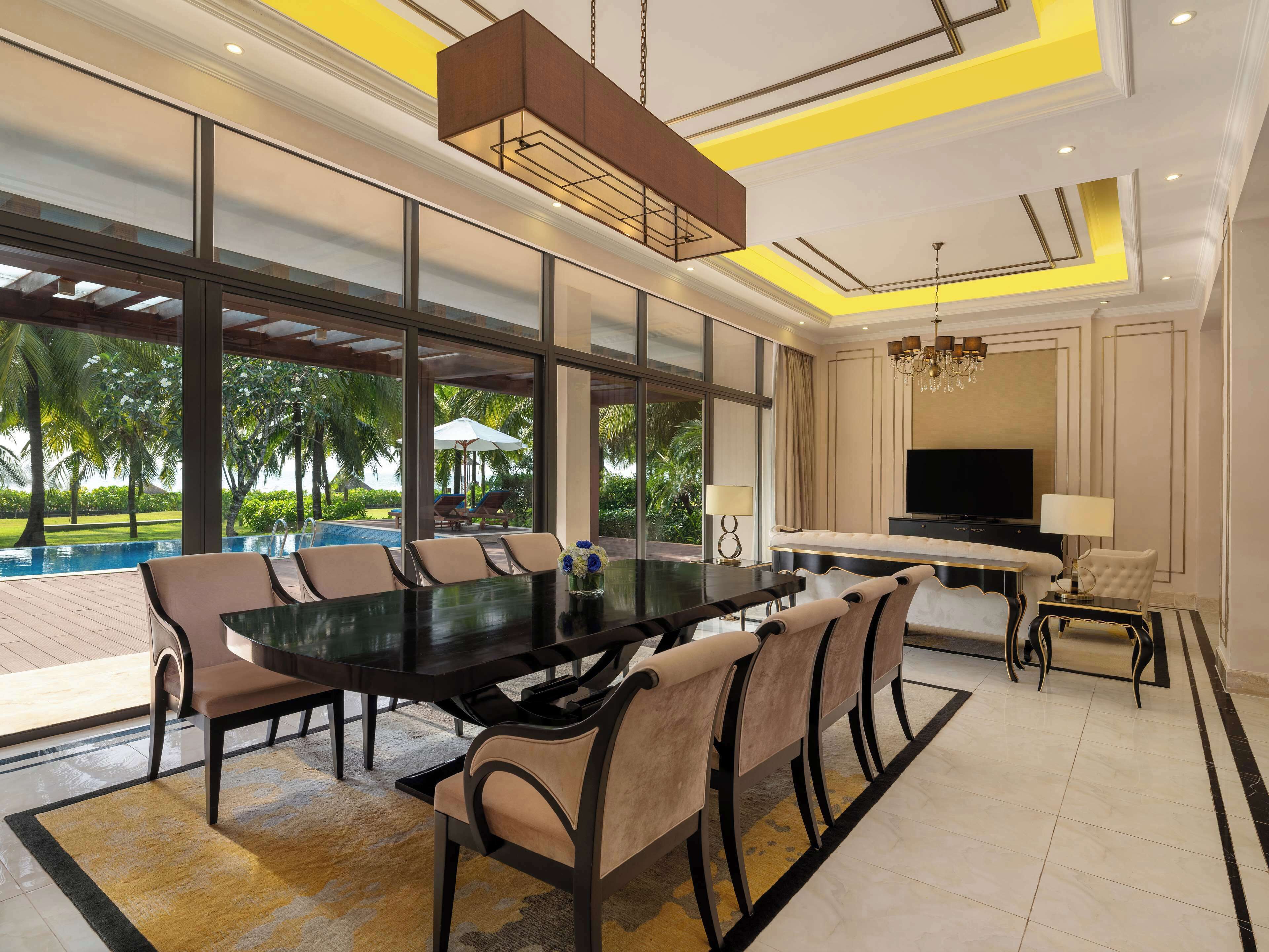 Uma ampla área de jantar com uma mesa grande e cadeiras, televisão e vista para a piscina.