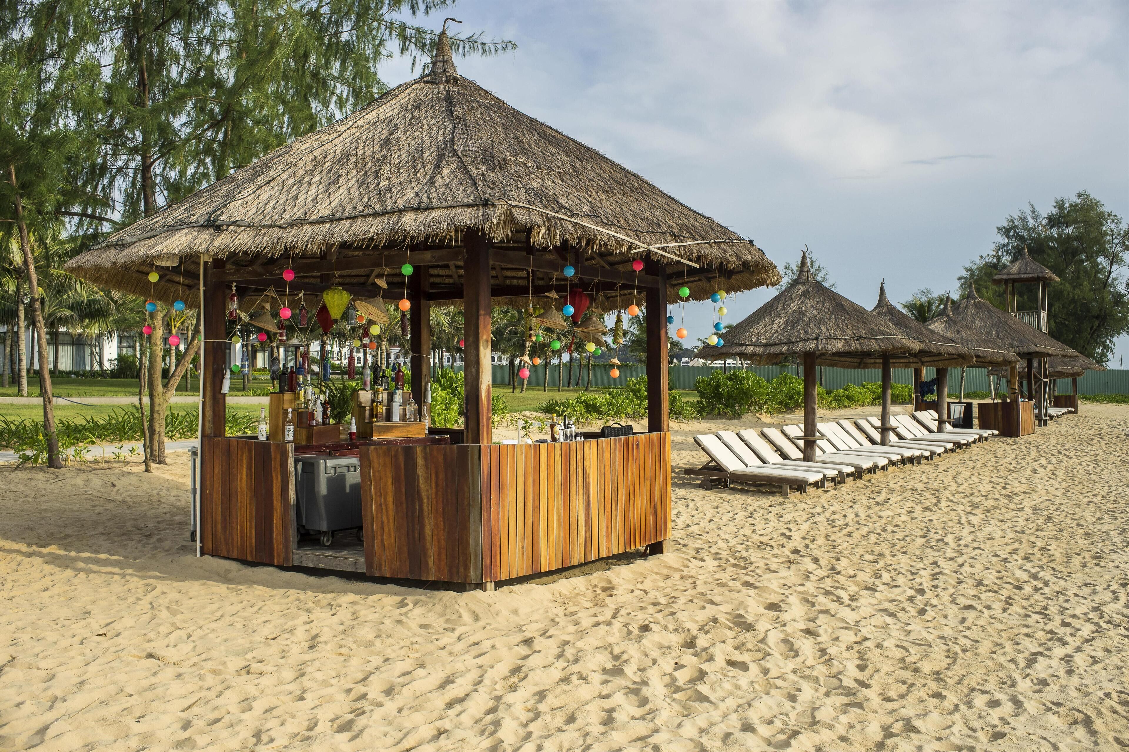 A beachside bar with thatched umbrellas and lounge chairs.