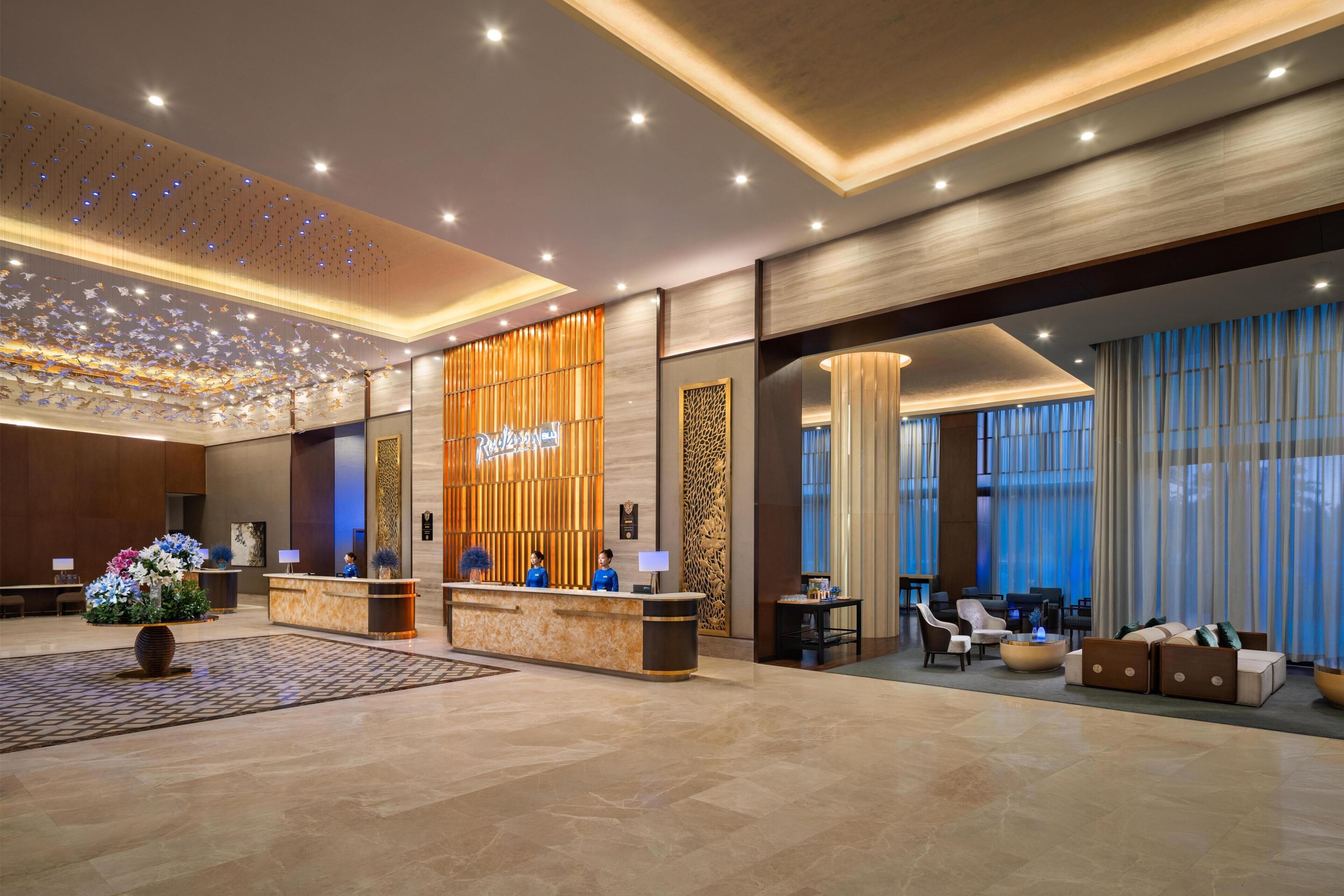 A hotel lobby with a reception desk, seating area, and large windows.