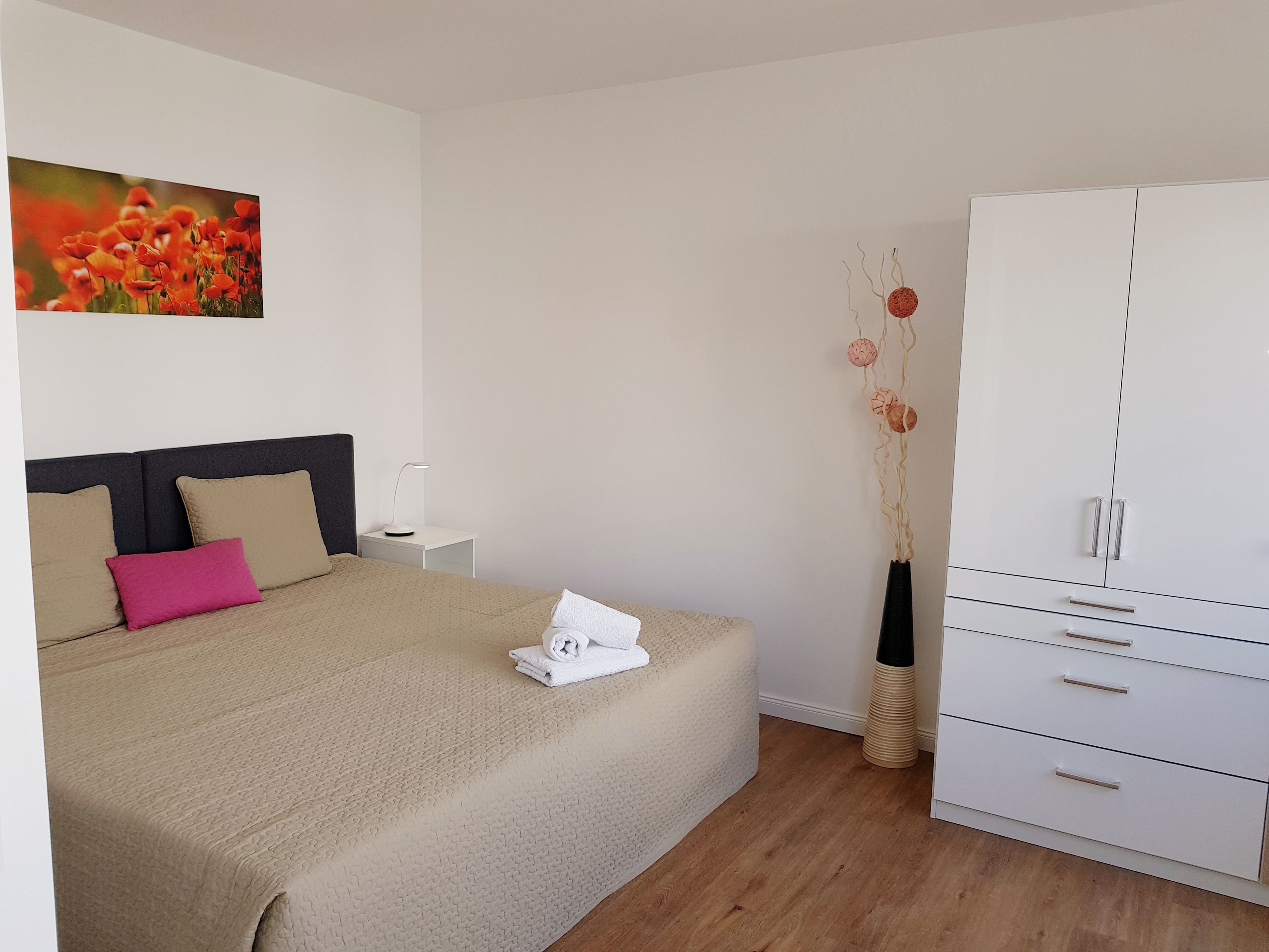 A neatly arranged bedroom with a bed, bedside table, lamp, and a wardrobe.