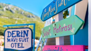 Un panneau indicateur comportant plusieurs panneaux de direction, notamment « DERIN MAVI SUIT OTEL » et « Soğut Hatinaz ».