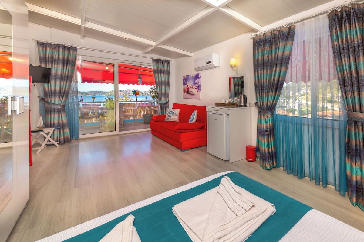 Een moderne woonkamer met een rode bank, een kleine kitchenette en uitzicht op zee door grote ramen.