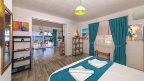 Une chambre d’hôtel avec un lit, un bureau, une chaise, une étagère, une fenêtre avec des rideaux et une vue sur la mer.