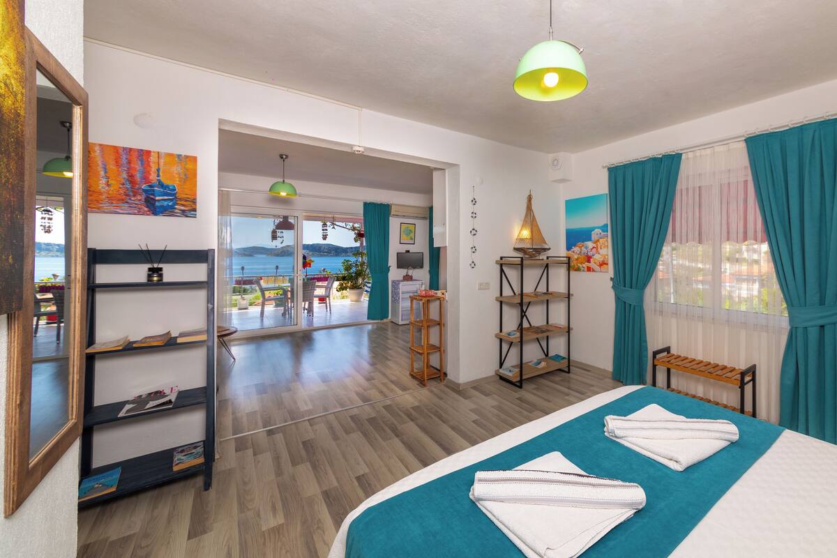 Hotelkamer met een bed, bureau, stoel, plank, raam met gordijnen en uitzicht op zee.